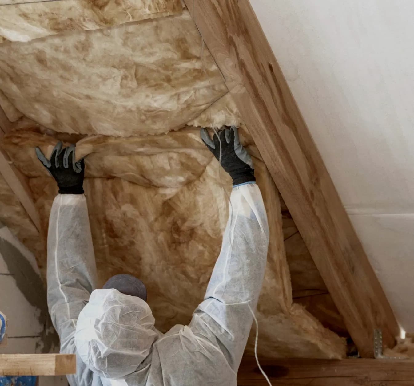 Worker in protective coveralls pulling old yellowed batts out of a roof space