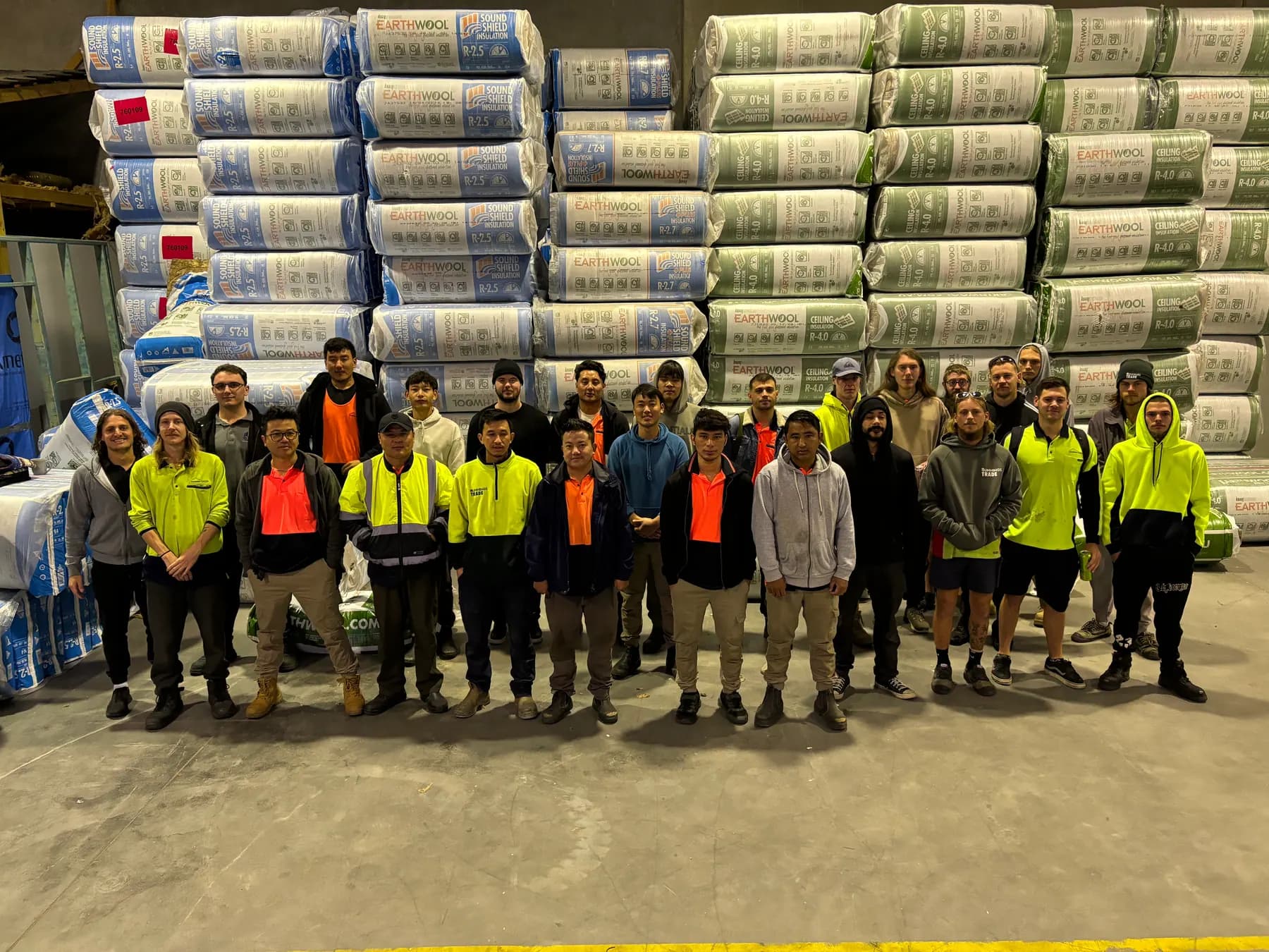 Insulation Extract crew standing in front of stacked insulation packs in a warehouse