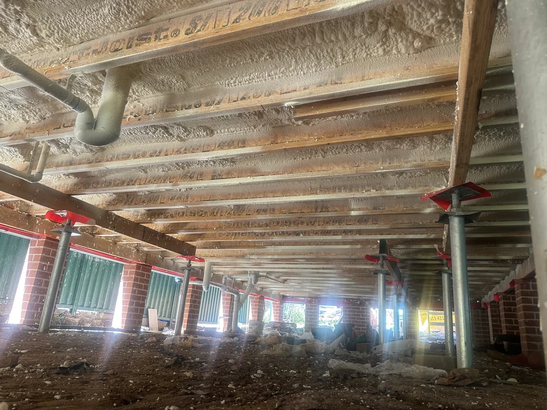 Subfloor beneath a raised home with spray foam applied to the underside of the floor