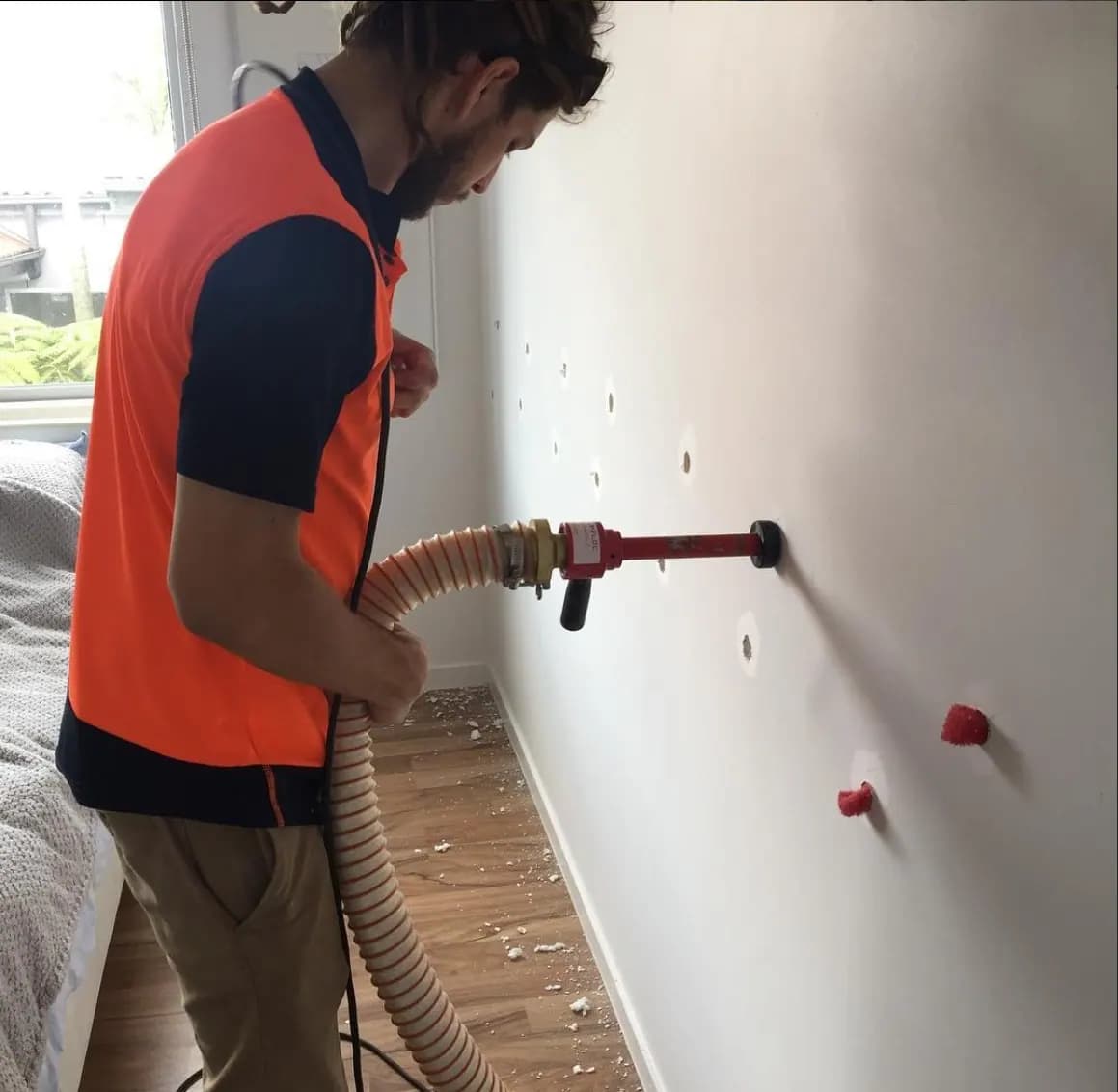 Installer blowing insulation into an internal wall through small drilled holes