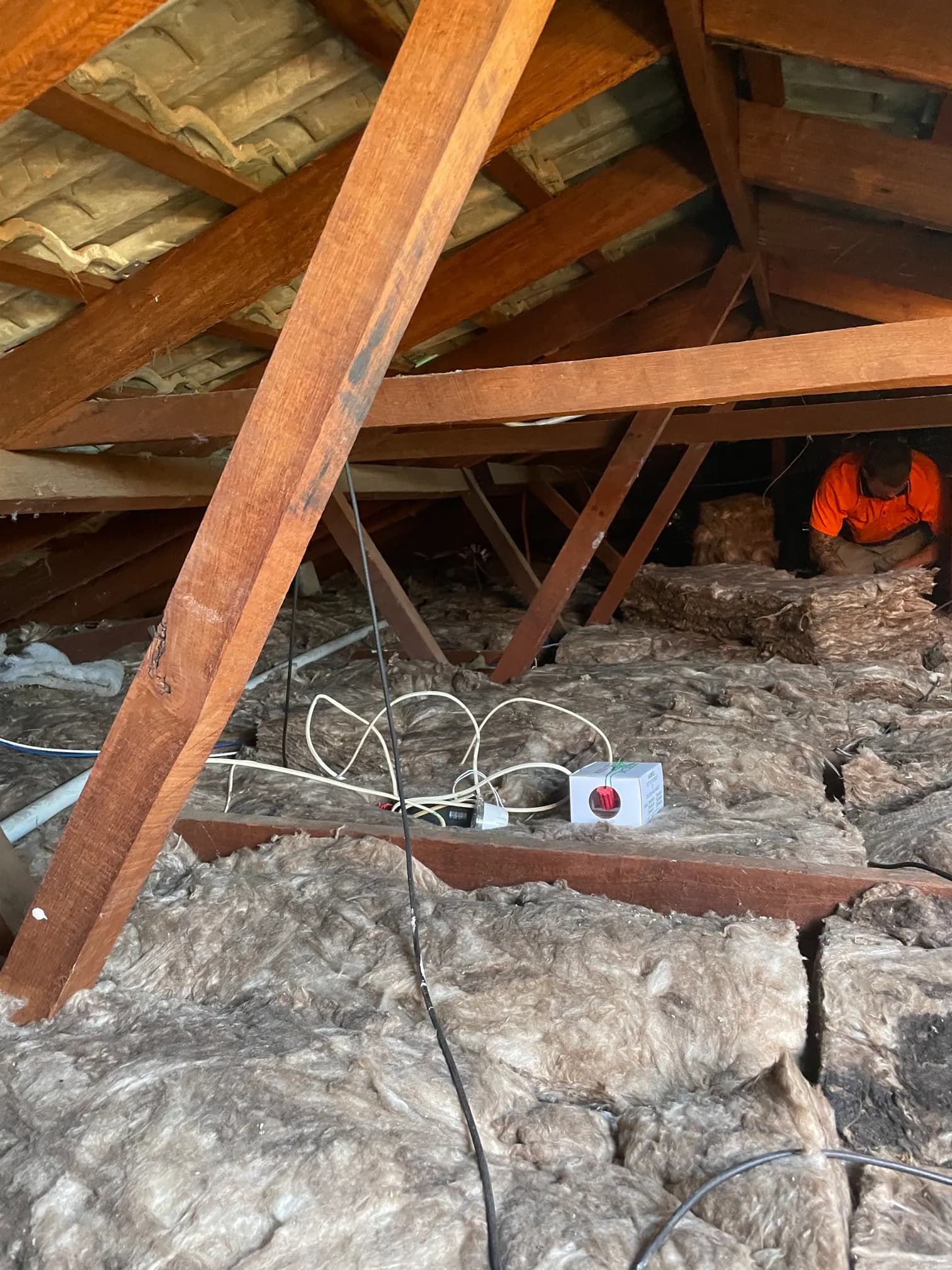 Installer fitting ceiling insulation batts inside a roof space