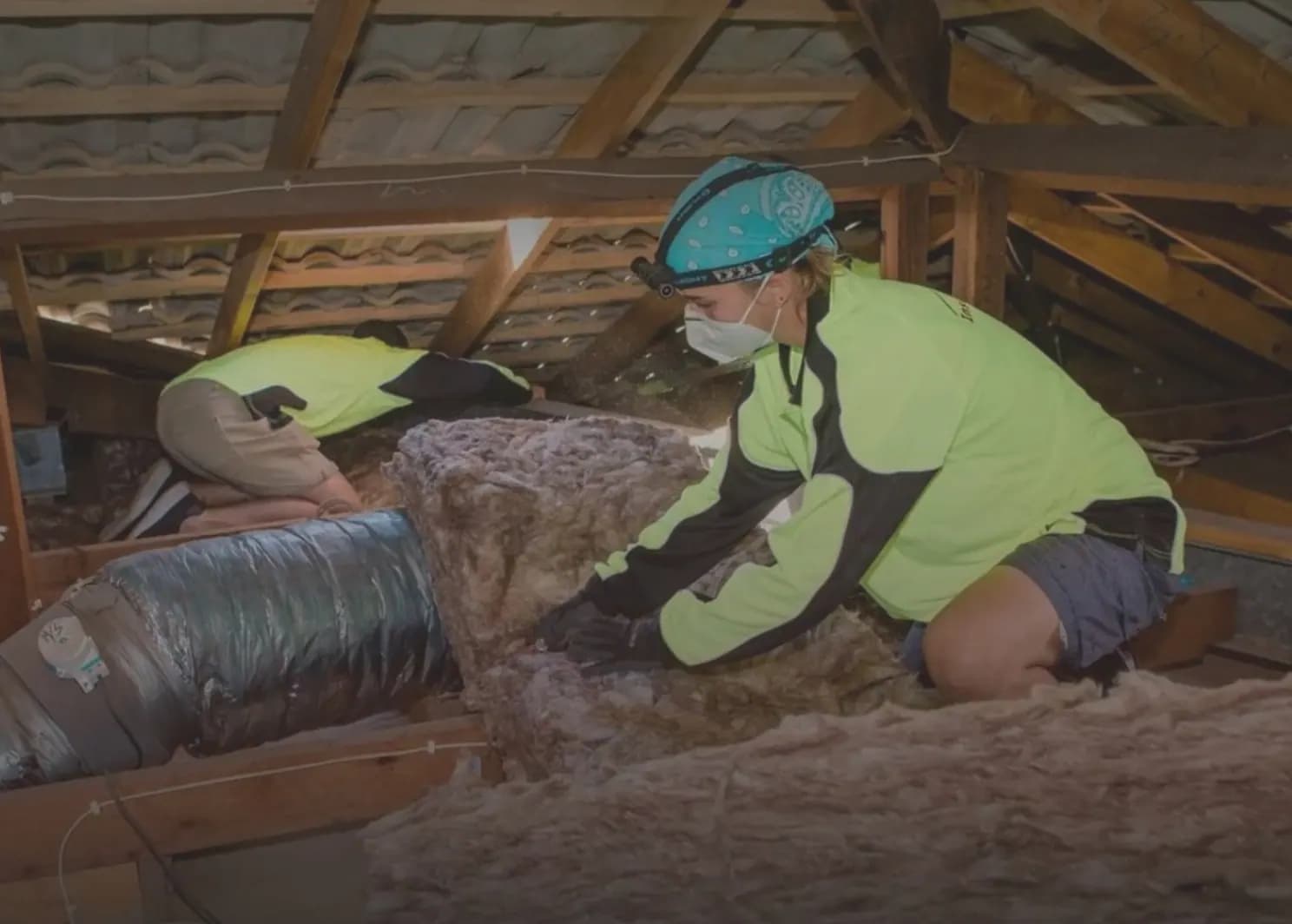 Technician in a respirator removing old insulation with a vacuum hose